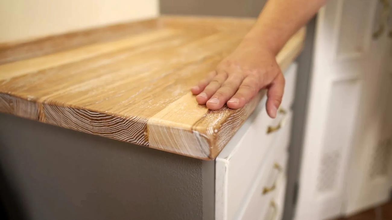 Hand berührt eine gebürstete und gekälkte Massivholz-Arbeitsplatte mit natürlicher Holzmaserung